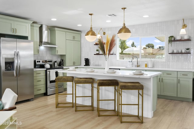 kitchen featuring wall chimney range hood, green cabinets, a breakfast bar area, a kitchen island, and appliances with stainless steel finishes