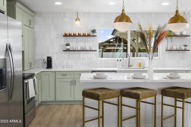 kitchen featuring green cabinets, a kitchen bar, stainless steel appliances, and hanging light fixtures