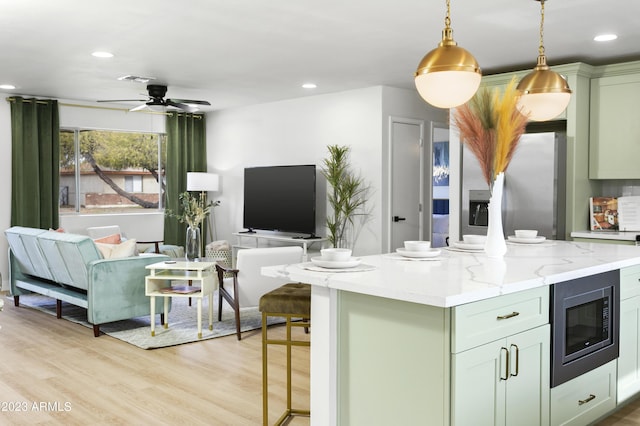 kitchen featuring a center island, light wood-type flooring, built in microwave, decorative light fixtures, and light stone counters