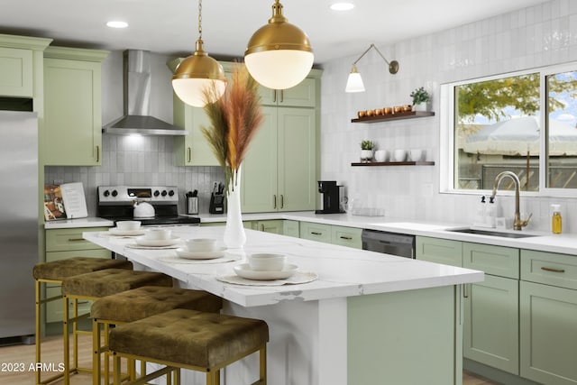 kitchen featuring a kitchen bar, stainless steel appliances, sink, wall chimney range hood, and green cabinets