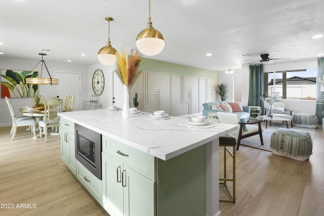 kitchen with ceiling fan, a center island, stainless steel microwave, and hanging light fixtures