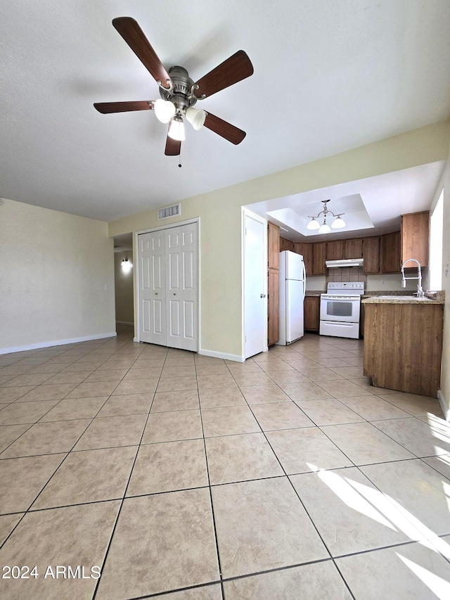 interior space featuring ceiling fan, light tile patterned floors, a raised ceiling, sink, and white appliances