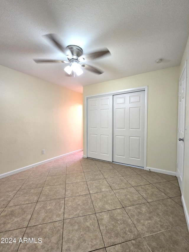 unfurnished bedroom with a closet, ceiling fan, a textured ceiling, and light tile patterned floors