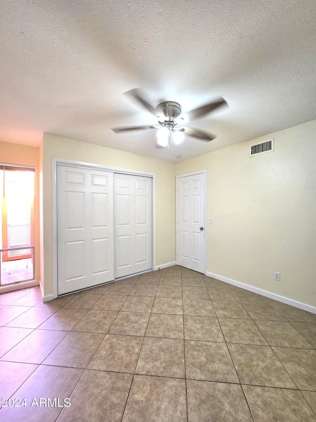 unfurnished bedroom featuring a closet, a textured ceiling, tile patterned floors, and ceiling fan