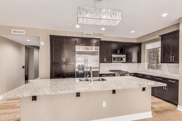 4805 N Woodmere Fairway Unit 1002, Scottsdale, AZ 85251 - kitchen with appliances with stainless steel finishes, a kitchen breakfast bar, light wood-style flooring, a center island with sink, and dark brown cabinetry