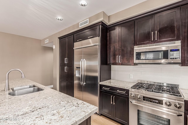 4805 N Woodmere Fairway Unit 1002, Scottsdale, AZ 85251 - kitchen with stainless steel appliances, decorative backsplash, light stone countertops, dark brown cabinets, and light wood-style flooring