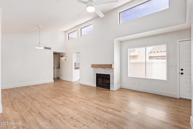 unfurnished living room featuring a high ceiling, ceiling fan, light wood finished floors, a fireplace, and baseboards