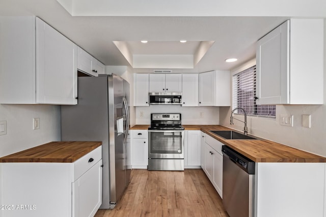 kitchen featuring wooden counters, stainless steel appliances, a sink, a raised ceiling, and recessed lighting
