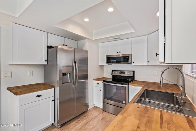 kitchen with wooden counters, appliances with stainless steel finishes, a sink, a raised ceiling, and white cabinetry