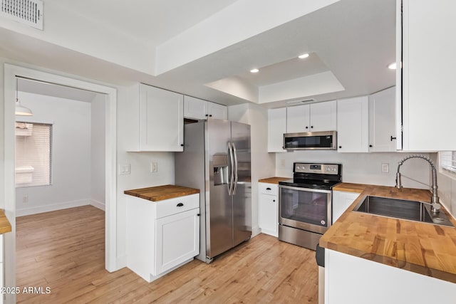 kitchen featuring wooden counters, appliances with stainless steel finishes, a sink, a raised ceiling, and light wood-type flooring