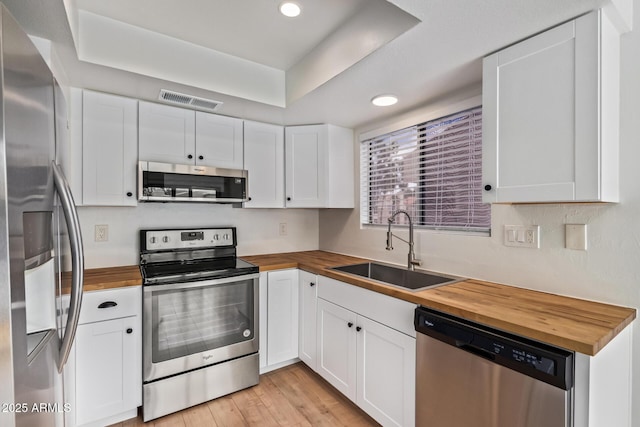 kitchen featuring butcher block countertops, stainless steel appliances, a sink, white cabinetry, and light wood finished floors