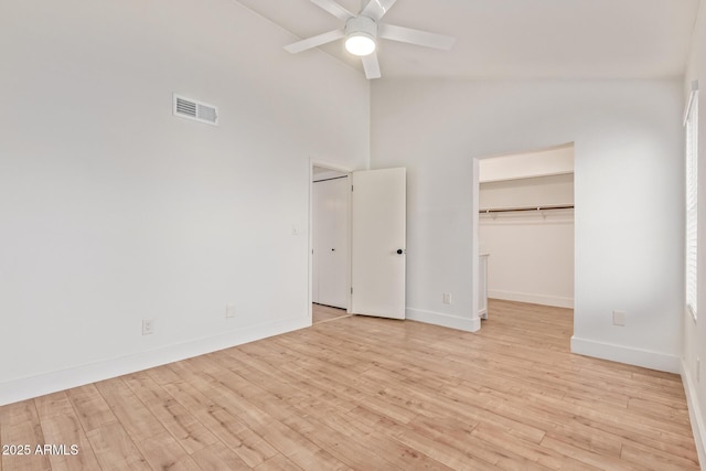 unfurnished bedroom featuring baseboards, light wood-type flooring, high vaulted ceiling, a spacious closet, and a ceiling fan