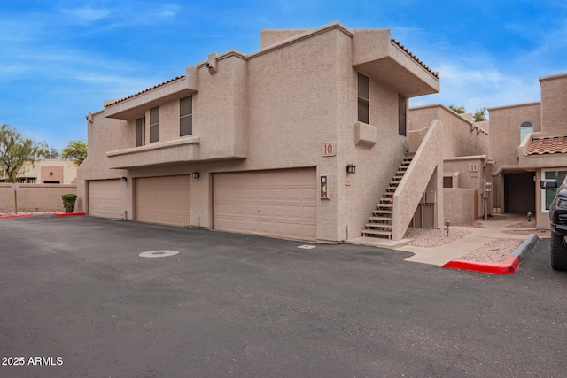 view of front of property with stucco siding, a garage, stairs, and a tiled roof