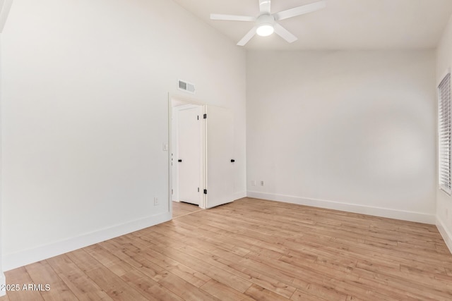 empty room with light wood-type flooring, a ceiling fan, baseboards, and high vaulted ceiling