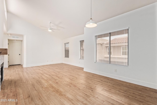 unfurnished living room with ceiling fan, vaulted ceiling, light wood finished floors, and baseboards
