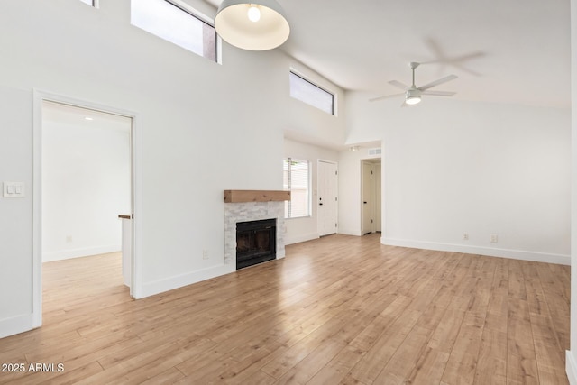 unfurnished living room featuring a ceiling fan, a towering ceiling, light wood-style floors, a fireplace, and baseboards