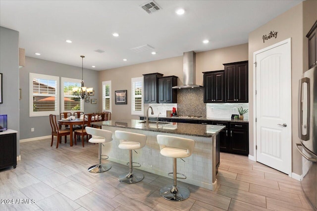 kitchen with sink, stainless steel appliances, wall chimney range hood, a breakfast bar area, and a kitchen island with sink