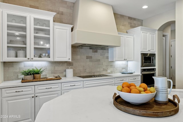 kitchen with premium range hood, backsplash, white cabinets, and appliances with stainless steel finishes