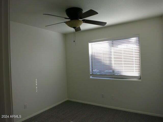 spare room featuring ceiling fan and dark carpet