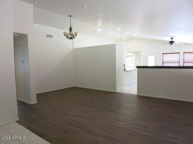 spare room featuring lofted ceiling, dark wood-type flooring, and ceiling fan with notable chandelier