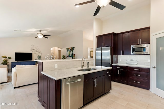 kitchen with sink, appliances with stainless steel finishes, dark brown cabinets, tasteful backsplash, and a center island with sink