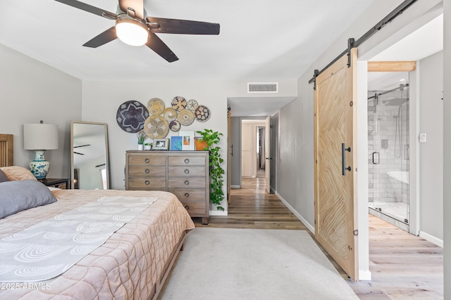 bedroom featuring a barn door, wood finished floors, baseboards, a ceiling fan, and ensuite bathroom