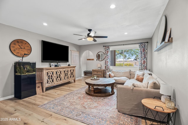 living room with arched walkways, recessed lighting, light wood-type flooring, a ceiling fan, and baseboards