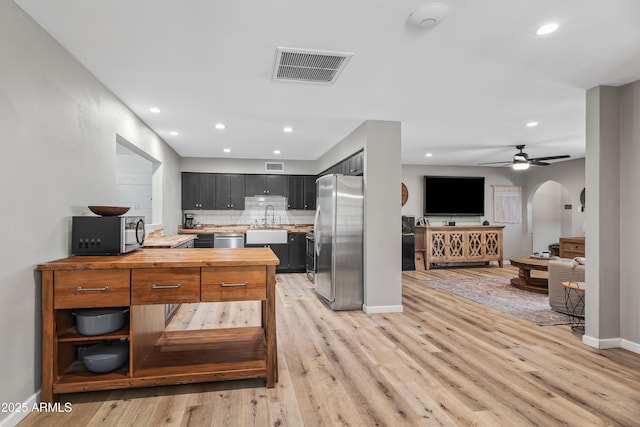 kitchen with appliances with stainless steel finishes, light wood-type flooring, wooden counters, arched walkways, and recessed lighting