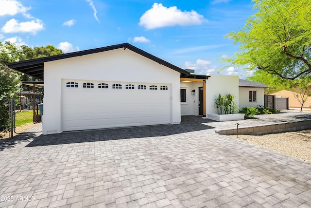 view of front of home featuring stucco siding, an attached garage, decorative driveway, and fence