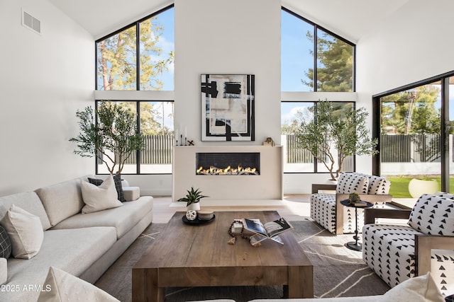 living room featuring a wealth of natural light, a glass covered fireplace, visible vents, and a high ceiling