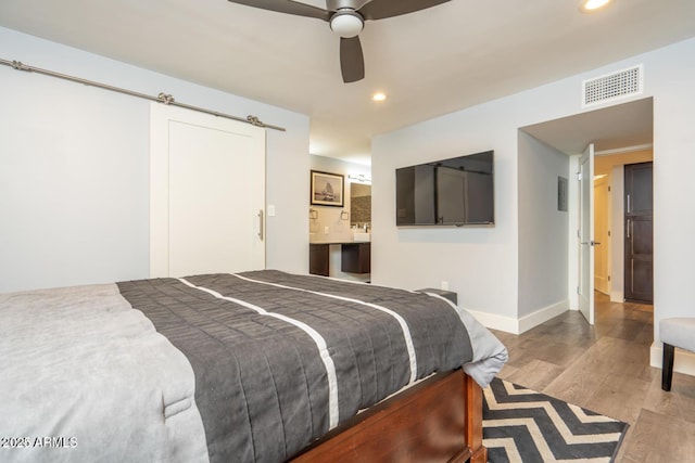 bedroom featuring a barn door, visible vents, baseboards, light wood-style floors, and recessed lighting