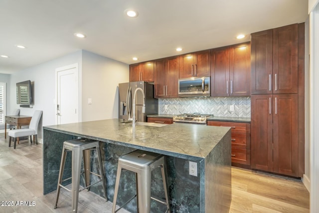 kitchen with light wood-style flooring, stainless steel appliances, tasteful backsplash, an island with sink, and a kitchen bar