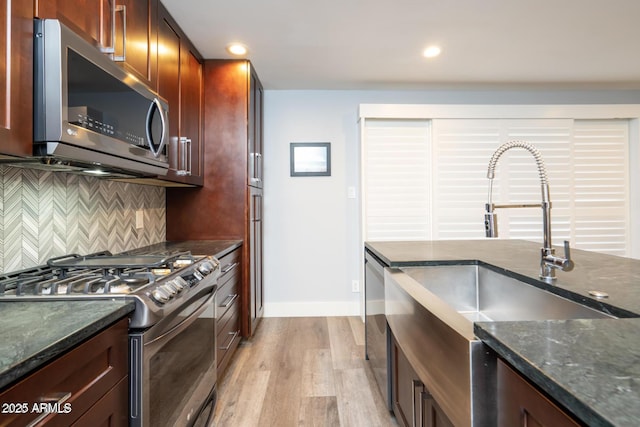 kitchen with tasteful backsplash, dark stone counters, light wood-style flooring, appliances with stainless steel finishes, and a sink