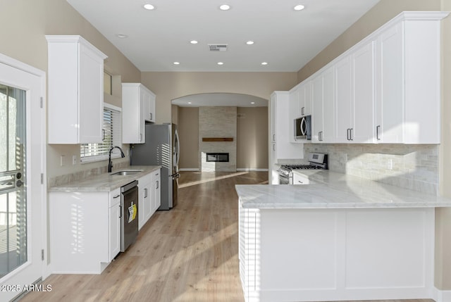 kitchen with light stone countertops, appliances with stainless steel finishes, white cabinetry, sink, and kitchen peninsula