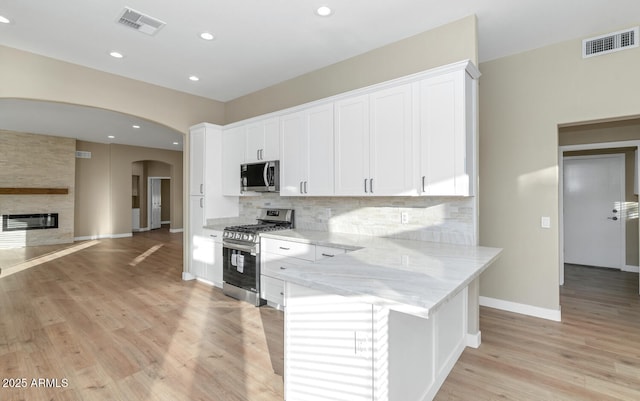 kitchen with light stone countertops, white cabinets, stainless steel appliances, a fireplace, and backsplash