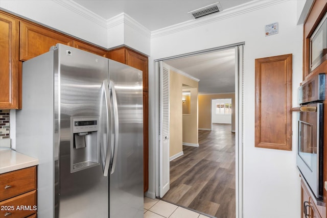 kitchen featuring crown molding, light hardwood / wood-style flooring, decorative backsplash, and appliances with stainless steel finishes