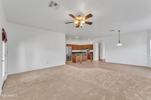 unfurnished living room featuring a ceiling fan, visible vents, arched walkways, a sink, and light carpet