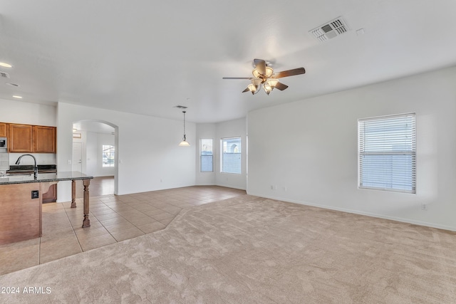 unfurnished living room with visible vents, light carpet, a ceiling fan, arched walkways, and light tile patterned floors