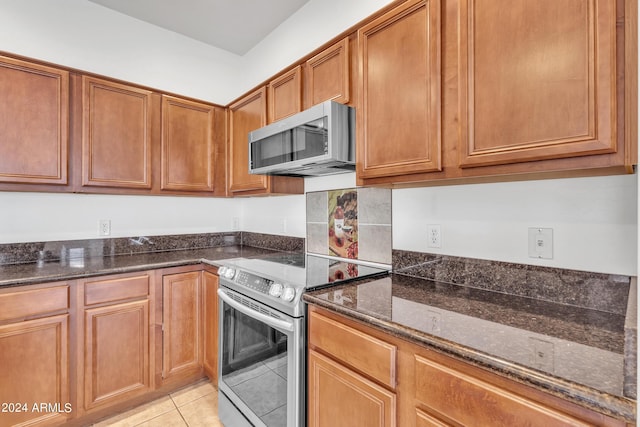 kitchen featuring dark stone countertops, light tile patterned flooring, brown cabinetry, and appliances with stainless steel finishes