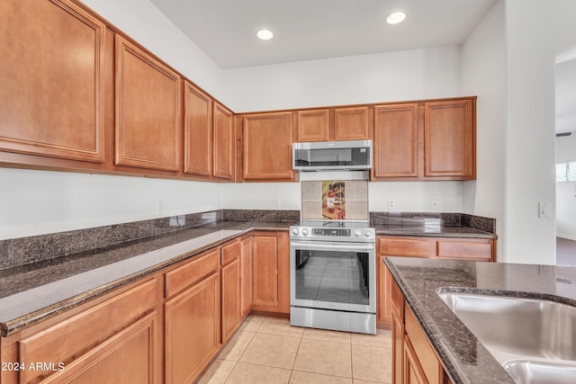 kitchen featuring brown cabinets, recessed lighting, stainless steel appliances, dark stone counters, and light tile patterned flooring