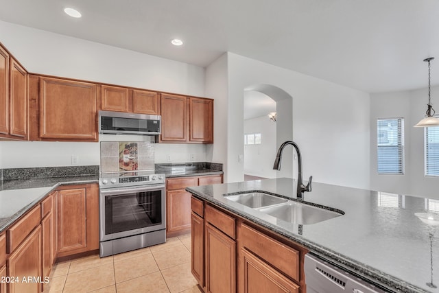 kitchen with light tile patterned floors, brown cabinetry, appliances with stainless steel finishes, and a sink