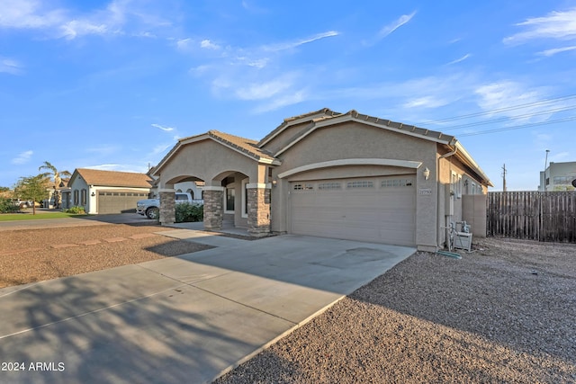 view of front facade with fence, a tile roof, concrete driveway, stucco siding, and an attached garage