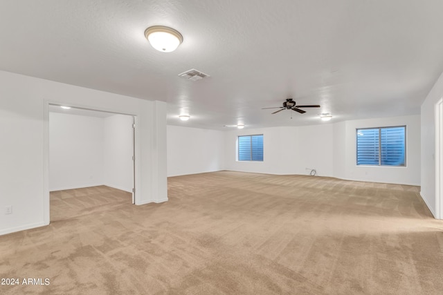 basement with visible vents, light carpet, a textured ceiling, and ceiling fan