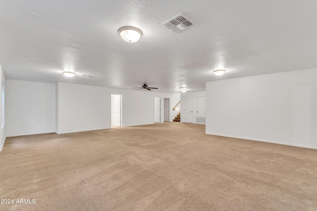 empty room featuring stairway, baseboards, visible vents, ceiling fan, and light carpet