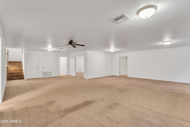 unfurnished room featuring a ceiling fan, stairway, light colored carpet, and visible vents