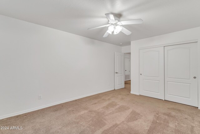 unfurnished bedroom with a closet, baseboards, light colored carpet, and a ceiling fan