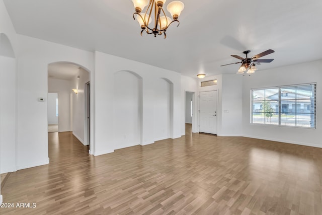 unfurnished living room featuring baseboards, arched walkways, wood finished floors, and ceiling fan with notable chandelier