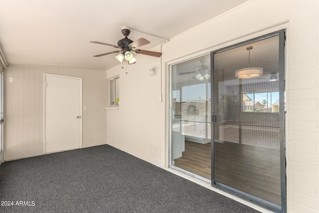 spare room featuring wood walls, ceiling fan, and dark carpet