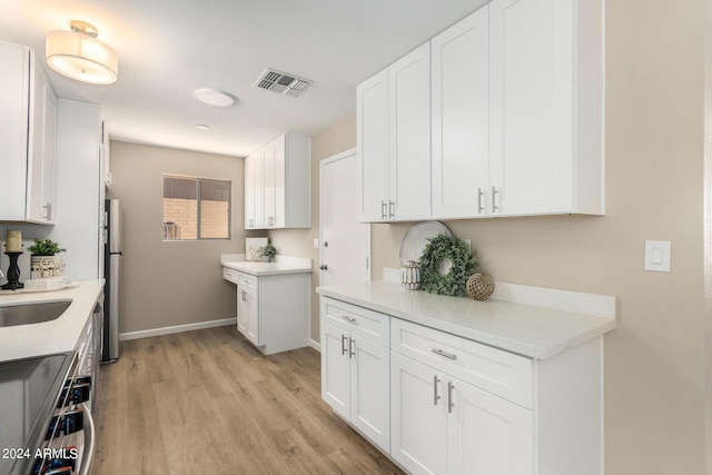 kitchen with sink, light hardwood / wood-style flooring, range, white cabinetry, and stainless steel refrigerator