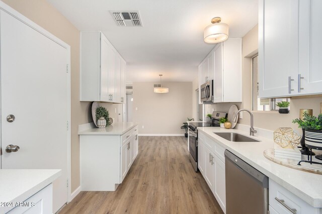 kitchen with appliances with stainless steel finishes, sink, light hardwood / wood-style flooring, white cabinets, and hanging light fixtures